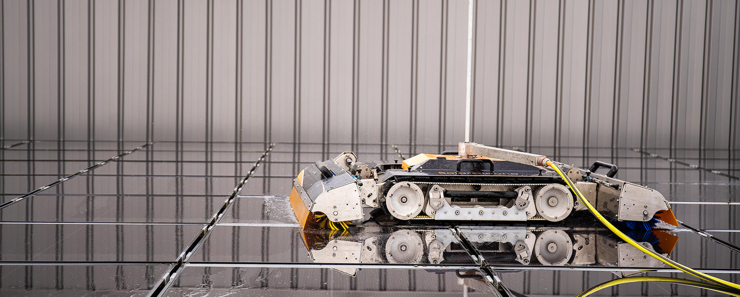 Side profile of SolarCleano F1 cleaning a solar panel, highlighting its compact body, tracks, and brush roller in contact with panel surface.